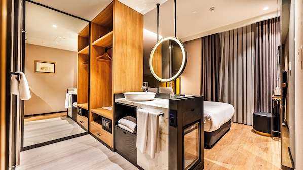 Une chambre d’hôtel moderne avec une armoire en bois, un miroir rond, un lavabo blanc et un lit doté d’une tête de lit noire.