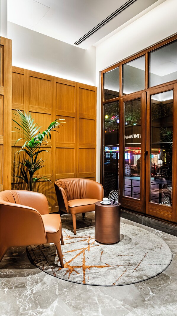 A lobby with wooden paneling, leather seating, a round coffee table, and a large glass door leading to a cafe. - Lamartine Hotel Istanbul (Istanbul)