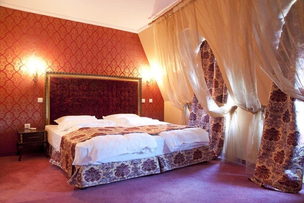 A hotel room with a large bed, a nightstand, and a wall-mounted lamp.