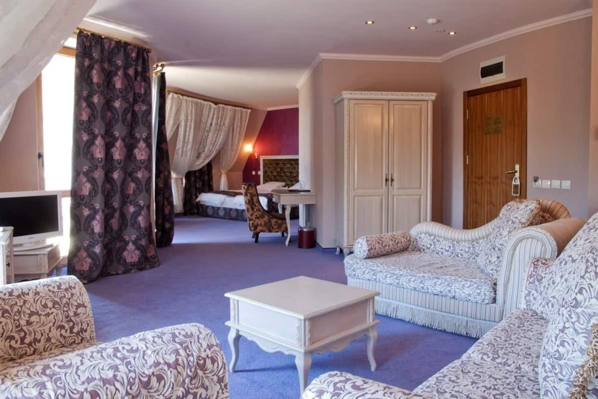 A hotel room with a large bed, a sitting area with patterned sofas, a television, and a wardrobe.