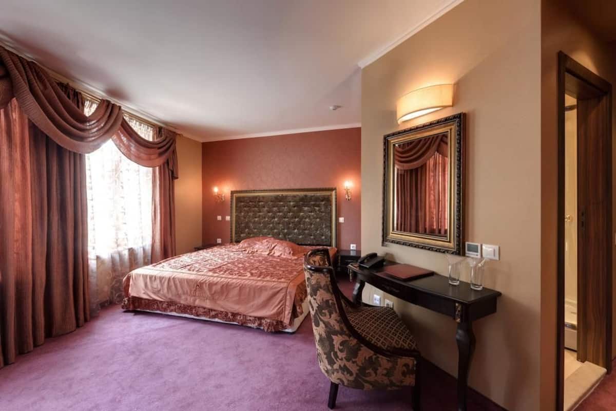 A hotel room with a large bed, a vanity with a mirror, and a door leading to another room.