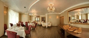 A spacious dining area with round tables and chairs, chandeliers, and a large mirror. - Kristel (Varna)