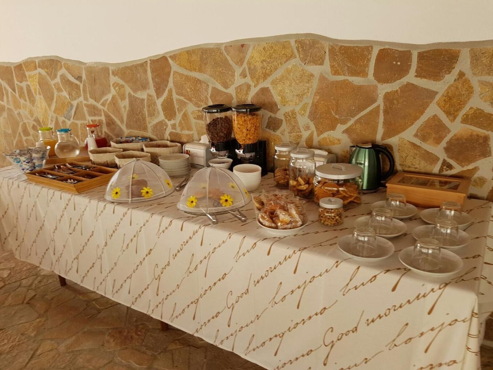 Un buffet de petit-déjeuner est installé sur une table, avec divers aliments et accompagnements, le tout adossé à un mur de pierre.