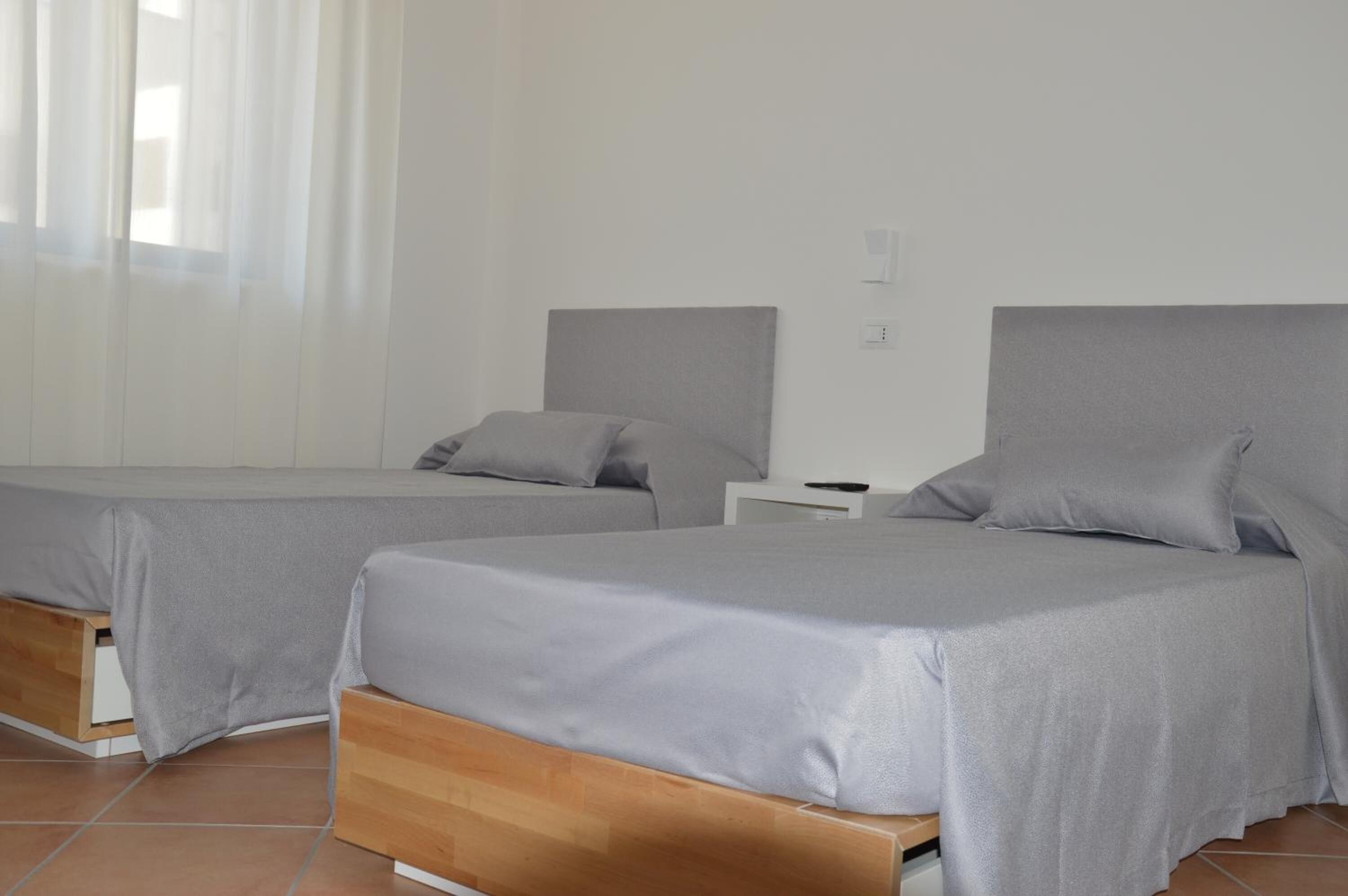 Une chambre avec deux lits simples, chacun doté d’une tête de lit en bois et d’une literie grise.