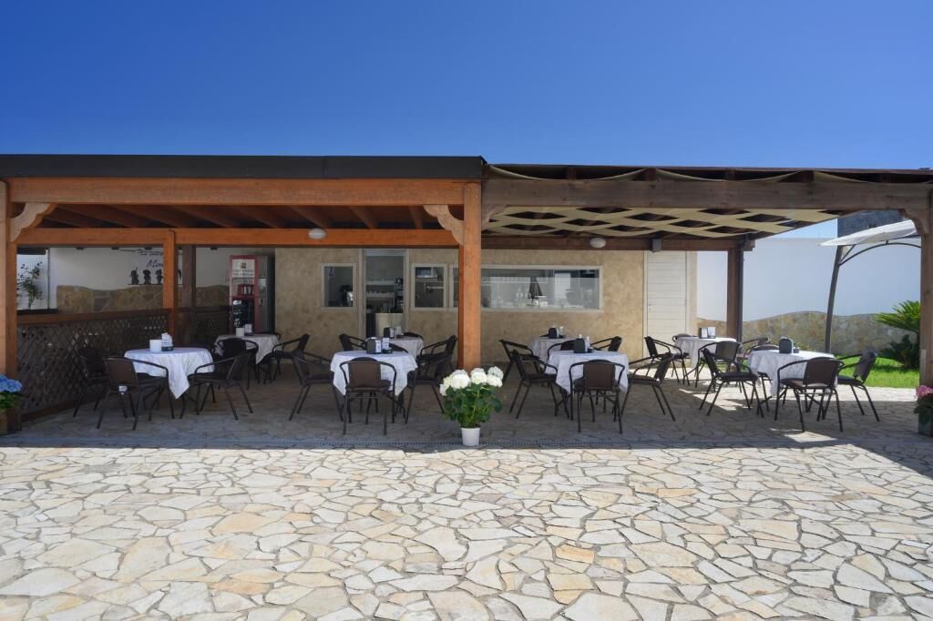 Eine Terrasse im Freien mit Steinboden und Esstischen, ausgestattet mit einer Pergola und Blick auf die Landschaft.