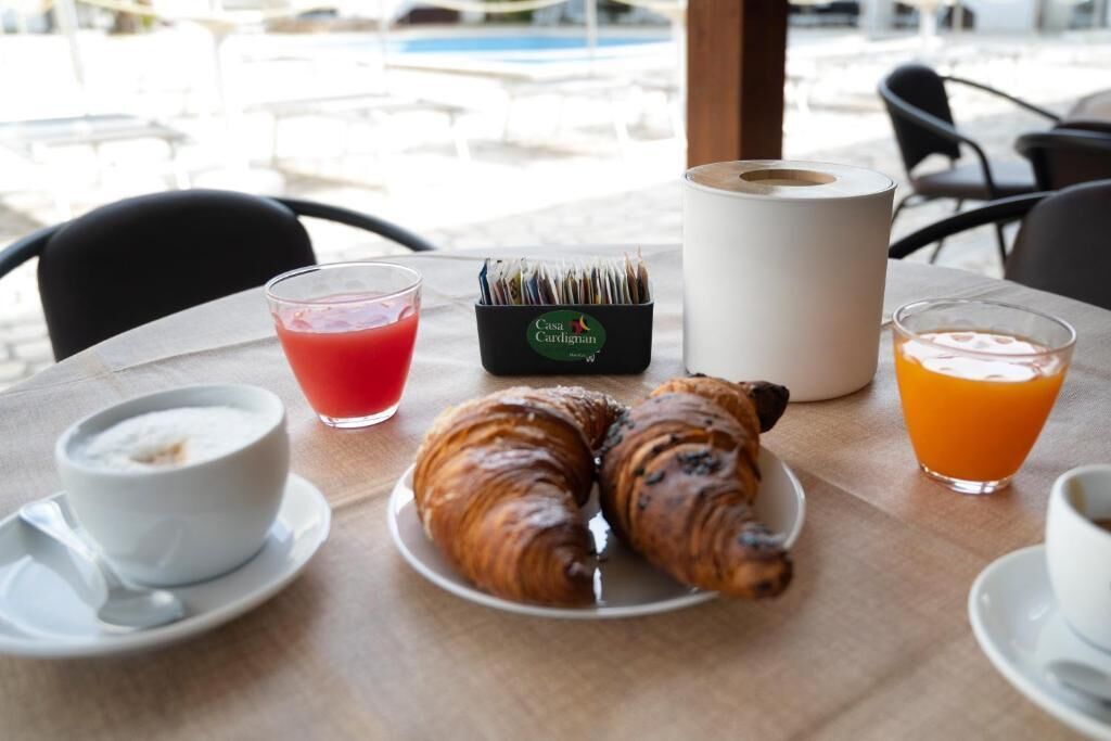 A breakfast table with croissants, a red drink, a white cup, a juice glass, and a magazine holder.