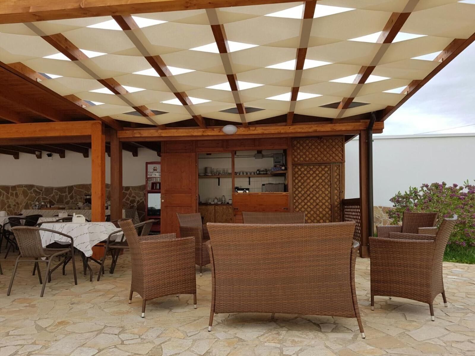 Una terrazza esterna con mobili in vimini, pavimento in pietra e una struttura in legno a pergola.