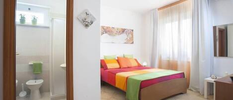 Una habitación de hotel con cama, baño y un amplio ventanal con cortinas.