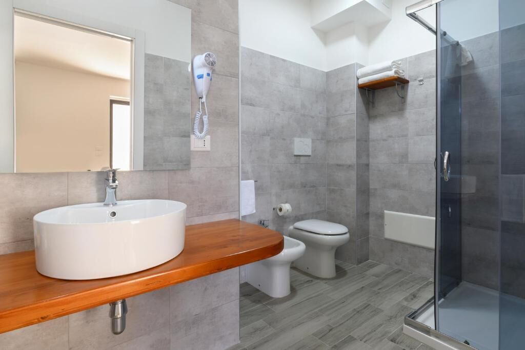 A bathroom with a white sink, a mirror, a hairdryer, a toilet, and a glass shower enclosure.