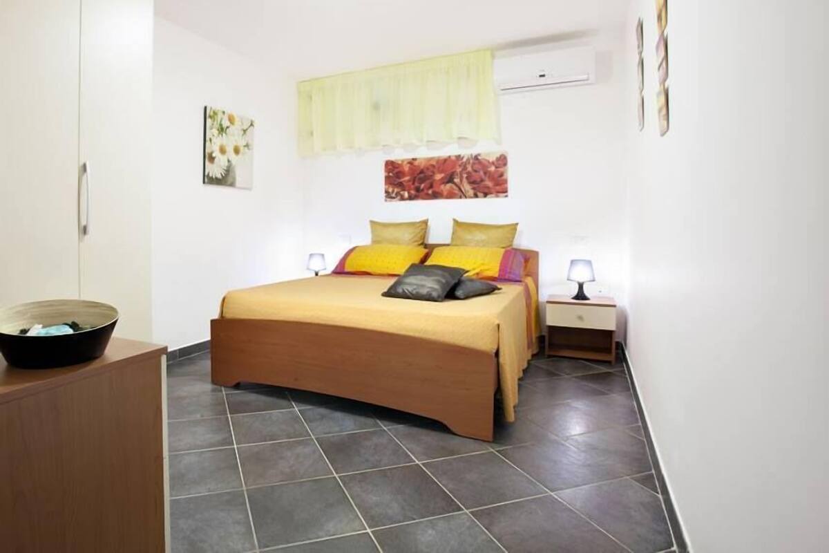 Ein Schlafzimmer mit einem Bett, einem Nachttisch, einer Lampe, einem Kleiderschrank und einer Wand-Klimaanlage.