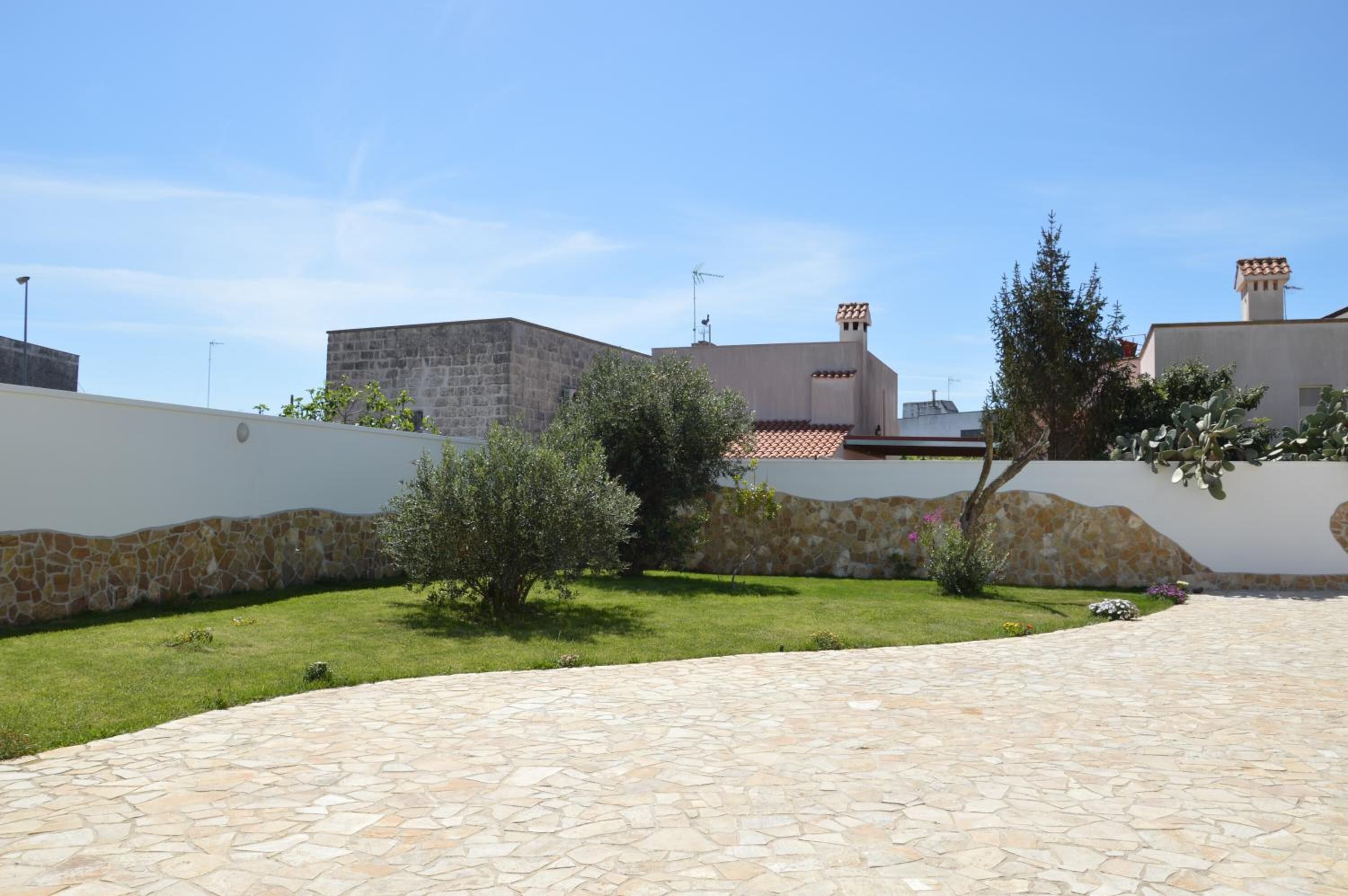 A courtyard with stone flooring, a low stone wall, and a grassy area with small trees.