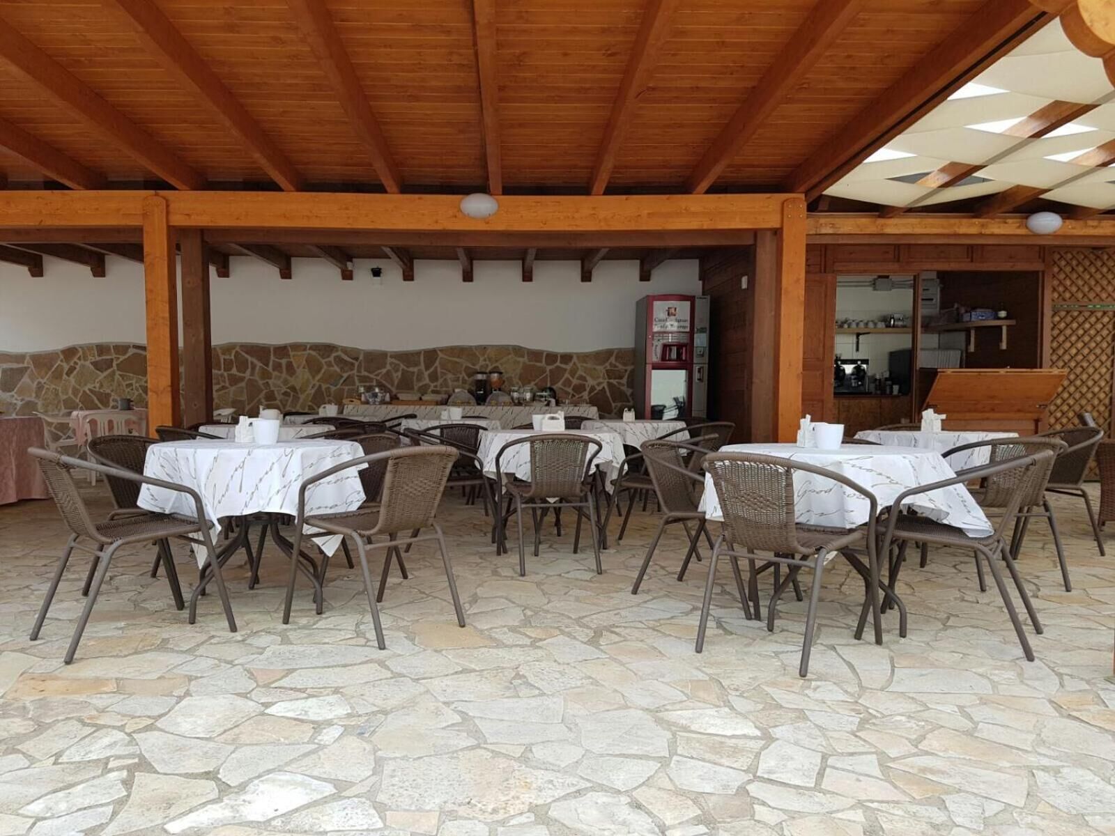 Un espace de restauration en plein air doté d’un sol en pierre, de chaises et de tables en osier recouvertes de nappes blanches.