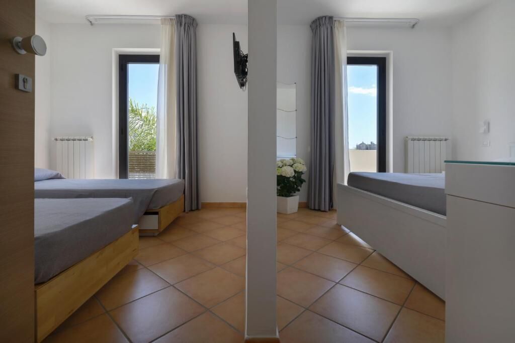 Een moderne slaapkamer met twee bedden, een witte ladekast en uitzicht op het omliggende landschap.