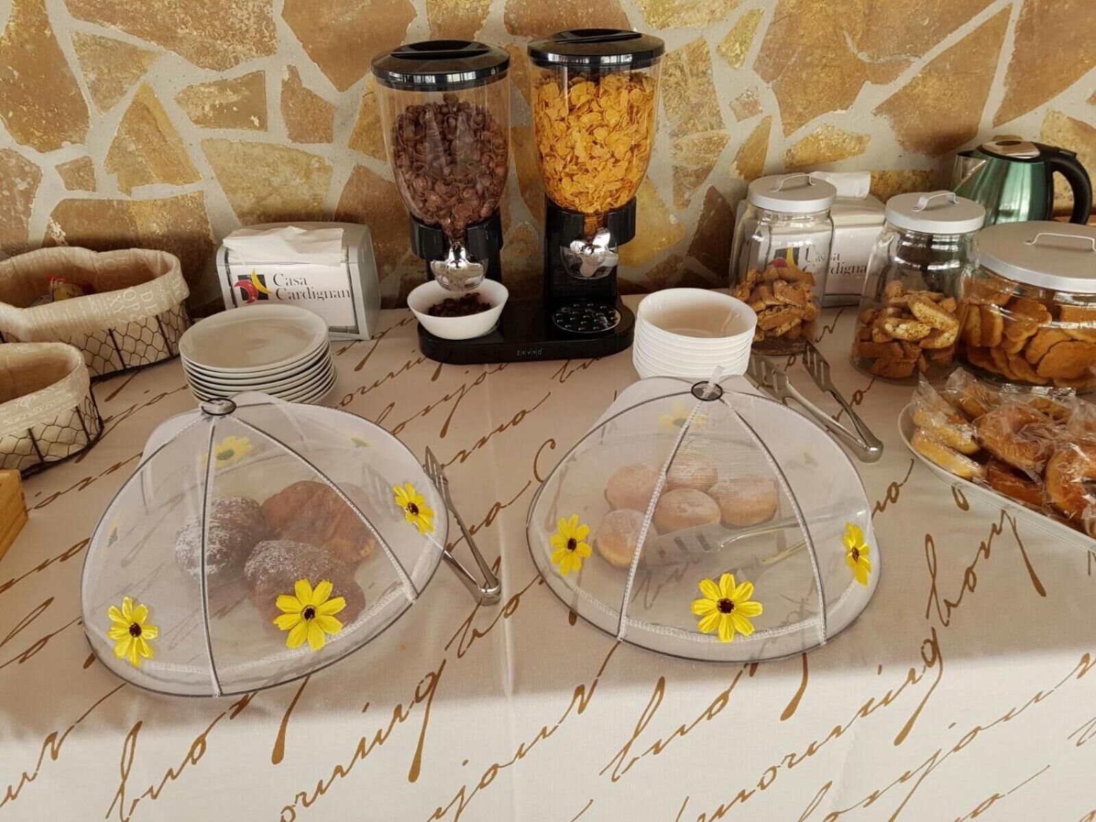A breakfast setup with two coffee makers, a blender, and various food items on a table.