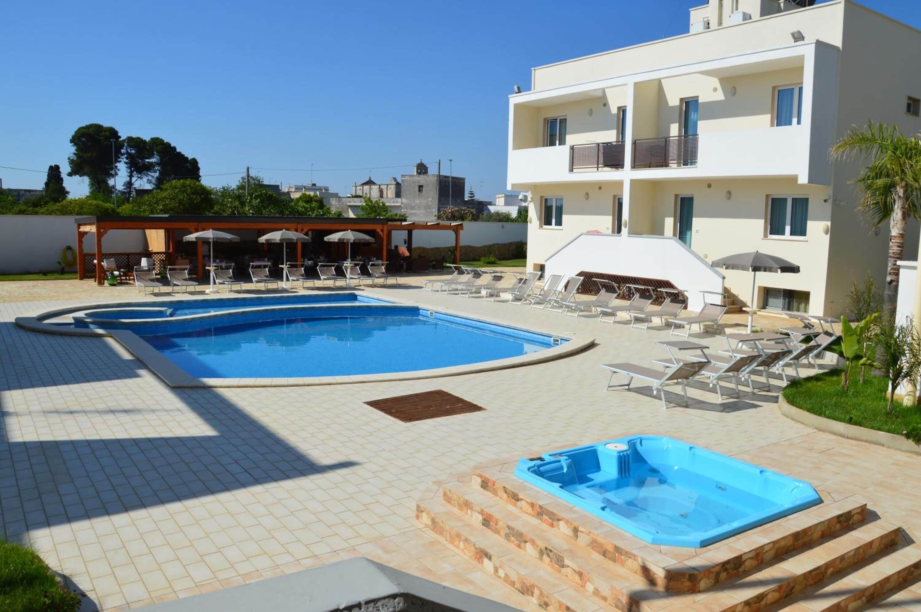 Un espace piscine avec des chaises longues et des parasols, un jacuzzi et un bâtiment doté de balcons.
