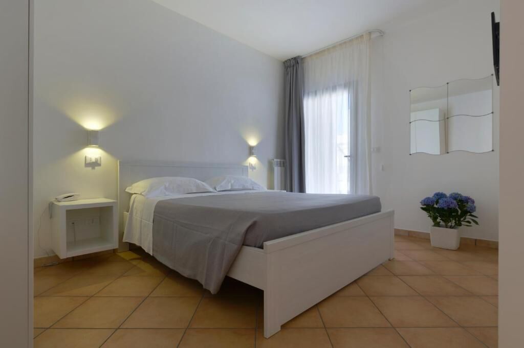 A bedroom with a bed, bedside tables, a nightstand, a potted plant, and a window with curtains.