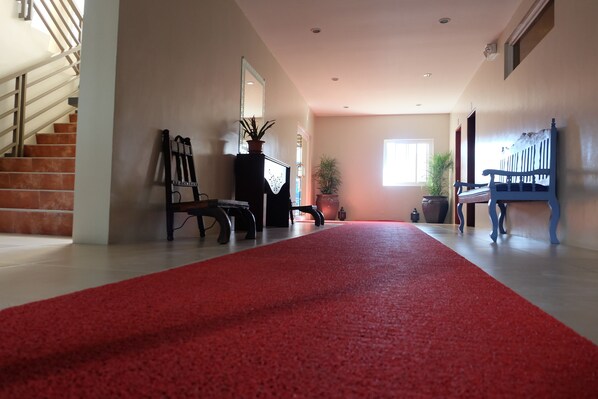 A hallway with a red carpet, a staircase, a wooden bench, and a potted plant.