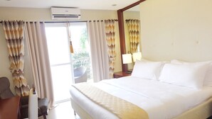 A hotel room with a large bed, a desk, a chair, a window with curtains, an air conditioning unit, and a nightstand with a lamp. - CML Beach Resort & Water Park (Lemery)