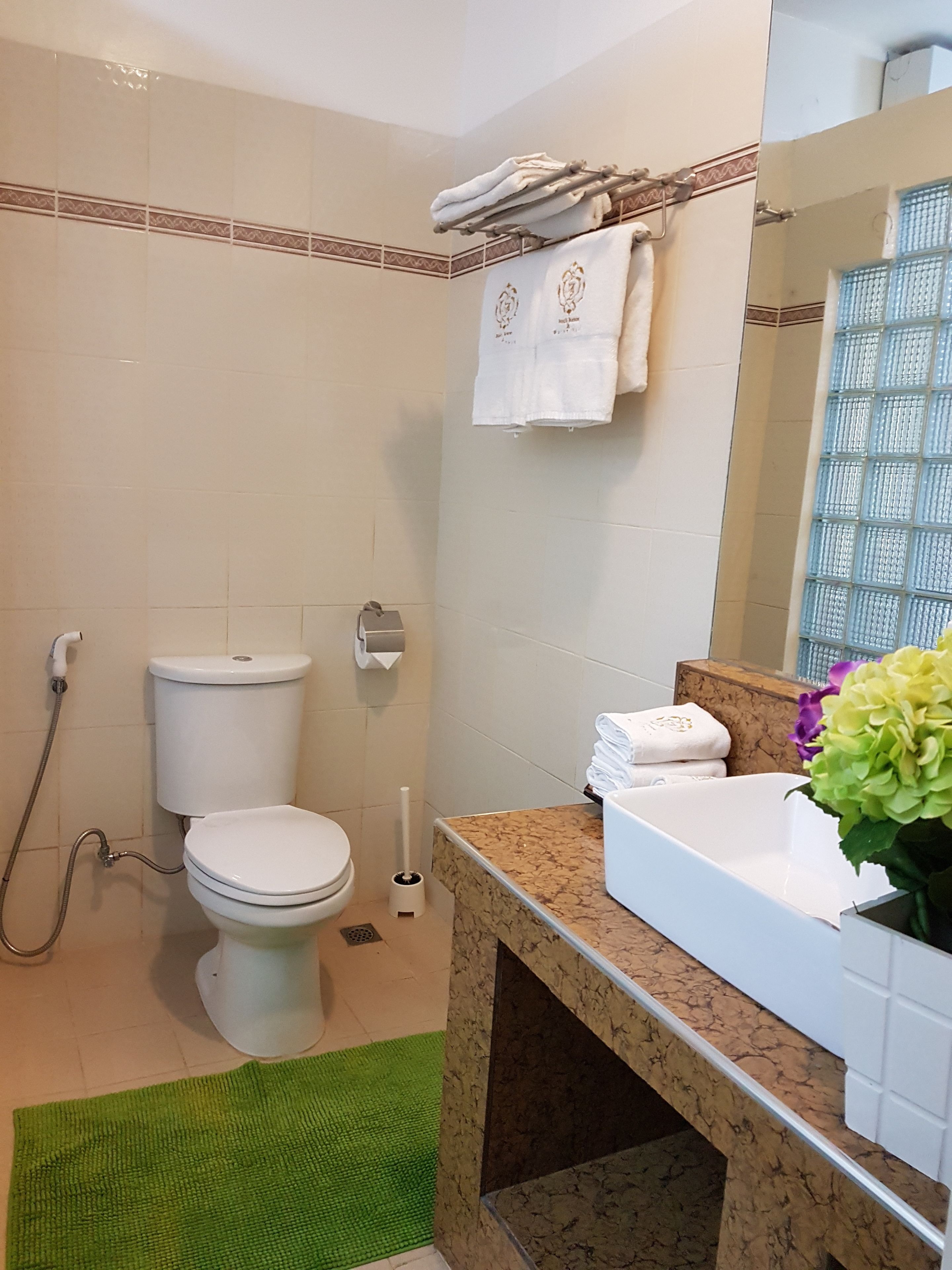 A bathroom with a toilet, a shower, a sink with a marble countertop, and a mirror.