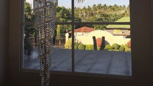 A room with a large window, a hanging crystal chandelier, and a view of palm trees and buildings outside. - CML Beach Resort & Water Park (Lemery)