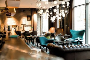 A modern interior with a bar area, seating with round tables, and a large window providing natural light. - Motel One Amsterdam-Waterlooplein (Amsterdam)