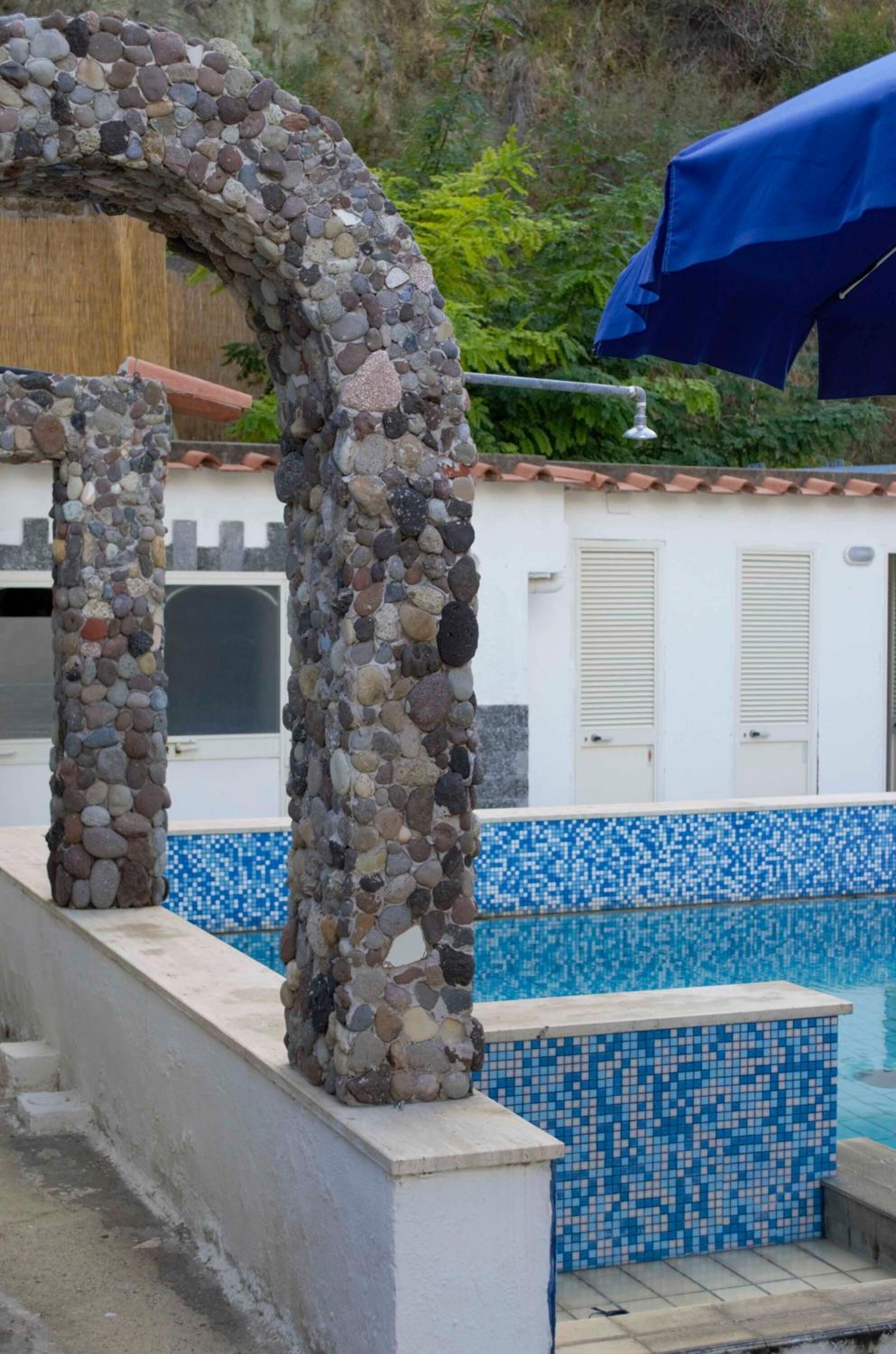 Un arco de piedra que da acceso a una zona de piscina con mosaicos azules.