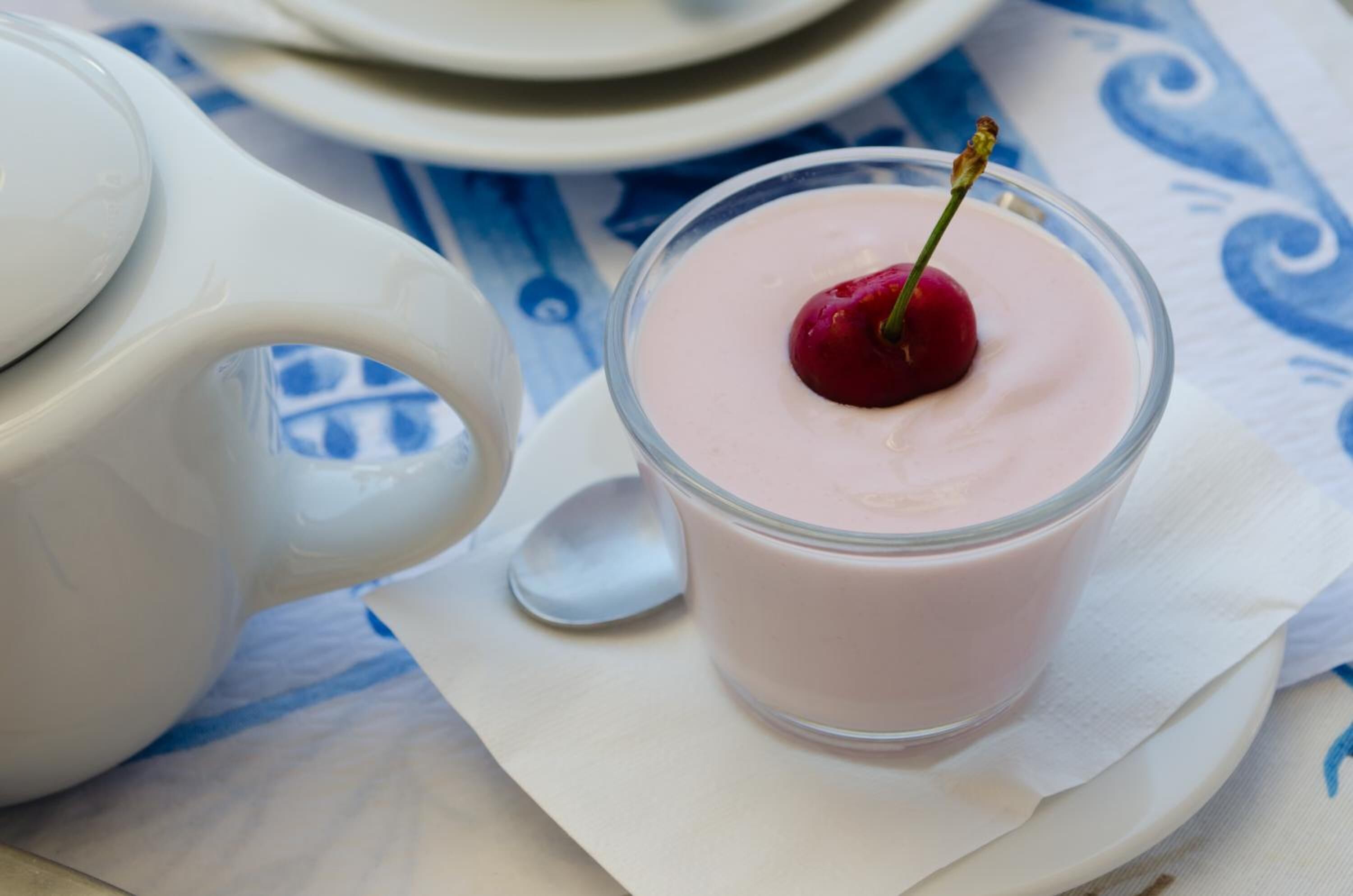 Un verre de dessert rose, surmonté d’une cerise, posé sur une serviette blanche.