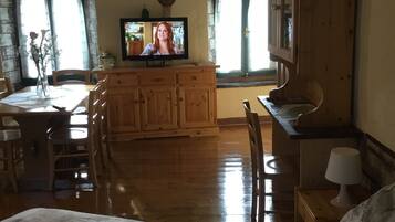 Ein gemütliches Zimmer mit einem hölzernen Bett, einem Esstisch aus Holz mit Stühlen, einem Fernseher und einer Holzkommode.