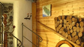 Una escalera de madera con barandilla de metal, una pared de piedra y una pared de madera con un mapa y leña apilada.