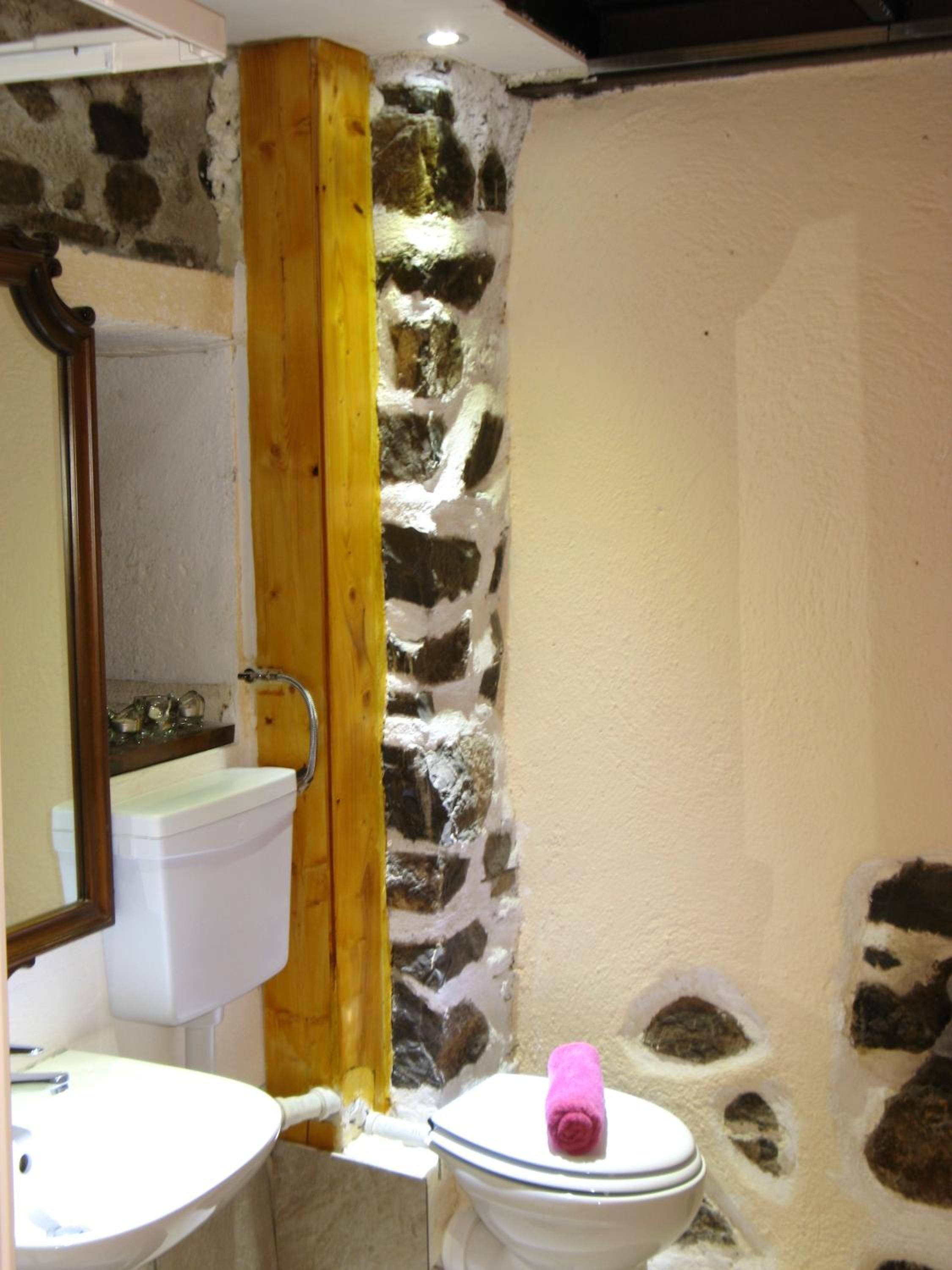 A bathroom with a stone wall, a wooden beam, a white toilet, and a sink with a mirror above it.
