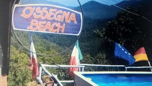 Señal que indica 'Ossegna Beach', con una piscina y sombrillas al fondo.