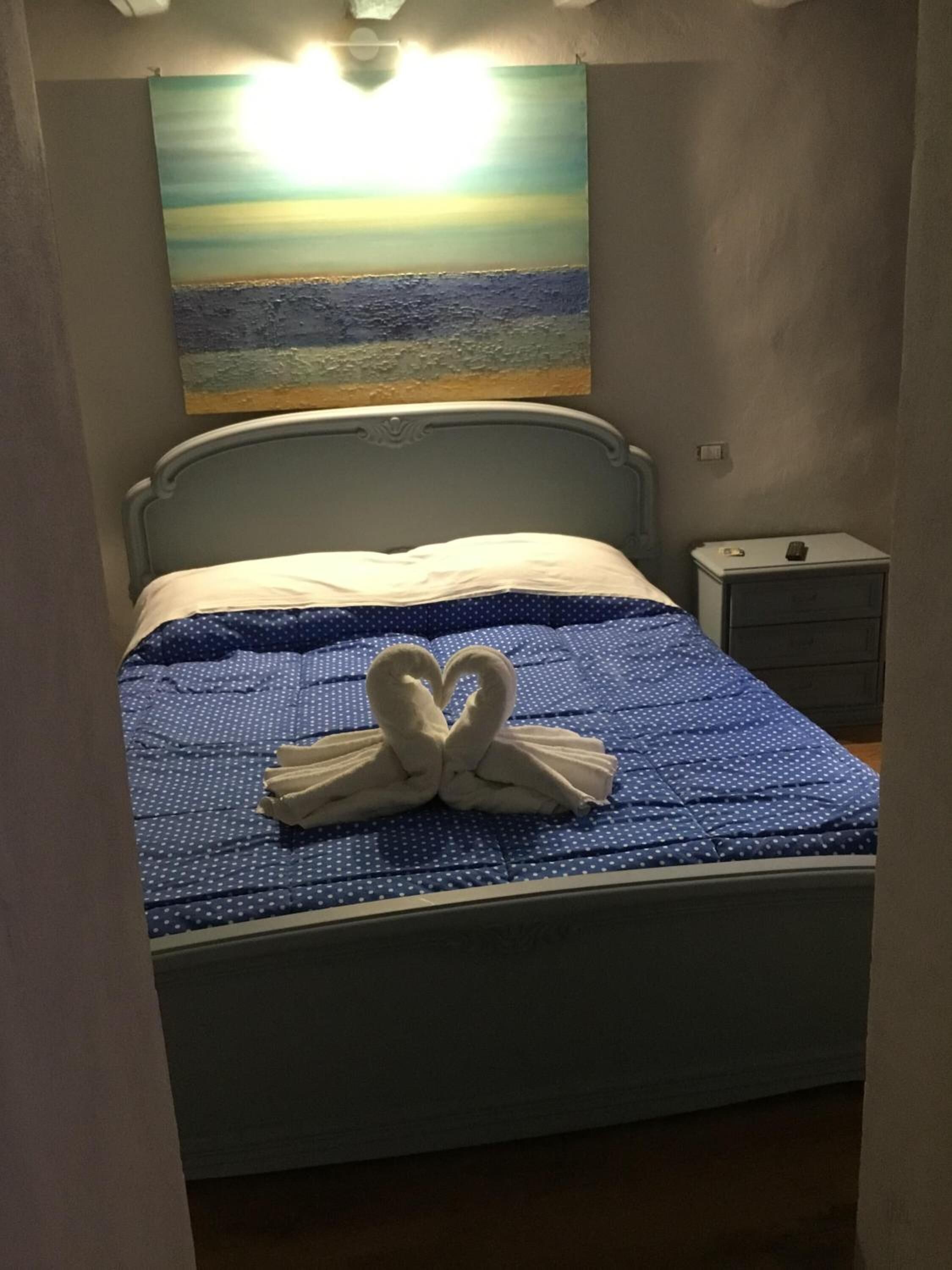 Ein ordentlich bezogenes Bett mit einer blau gepunkteten Tagesdecke und einer herzförmigen Handtuchgestaltung.