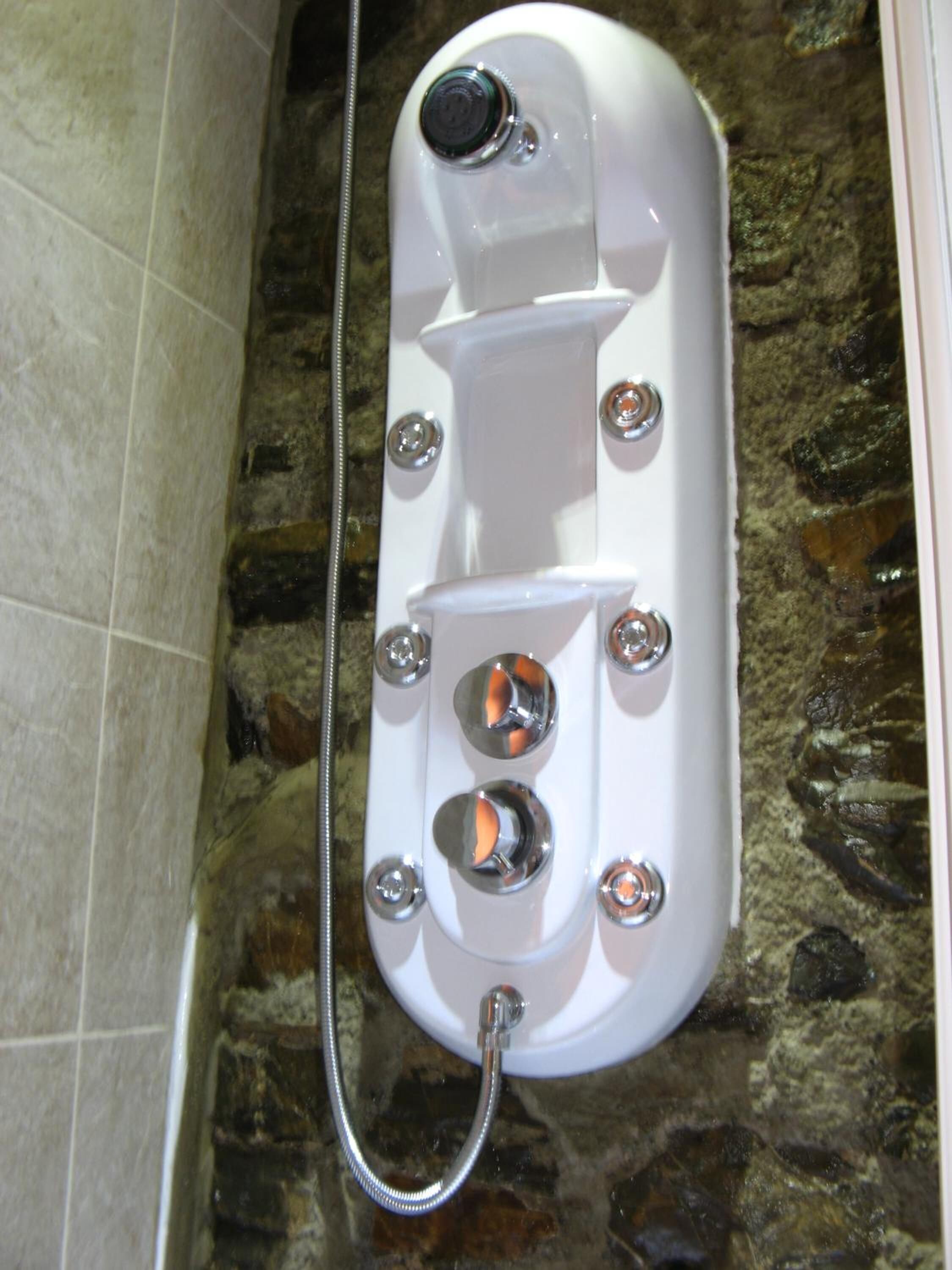 A white spa tub with a shower head, set against a stone wall.