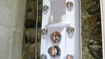 A white spa tub with a shower head, set against a stone wall.