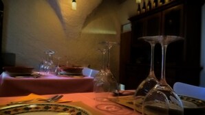 Una mesa dispuesta con platos, cubiertos y copas de vino en una habitación con poca luz y un ambiente rústico.