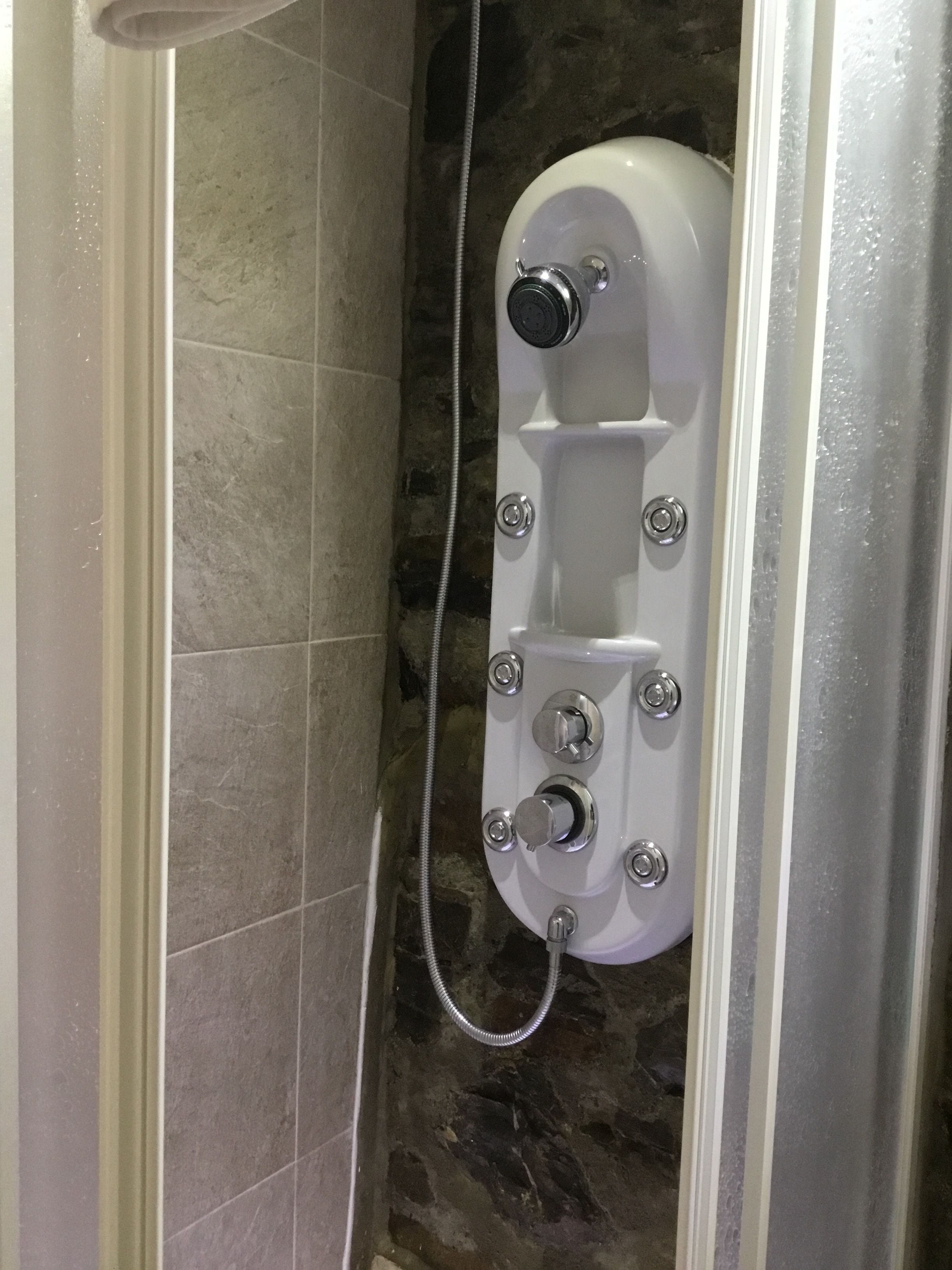 A shower enclosure with a control panel and a handheld showerhead.