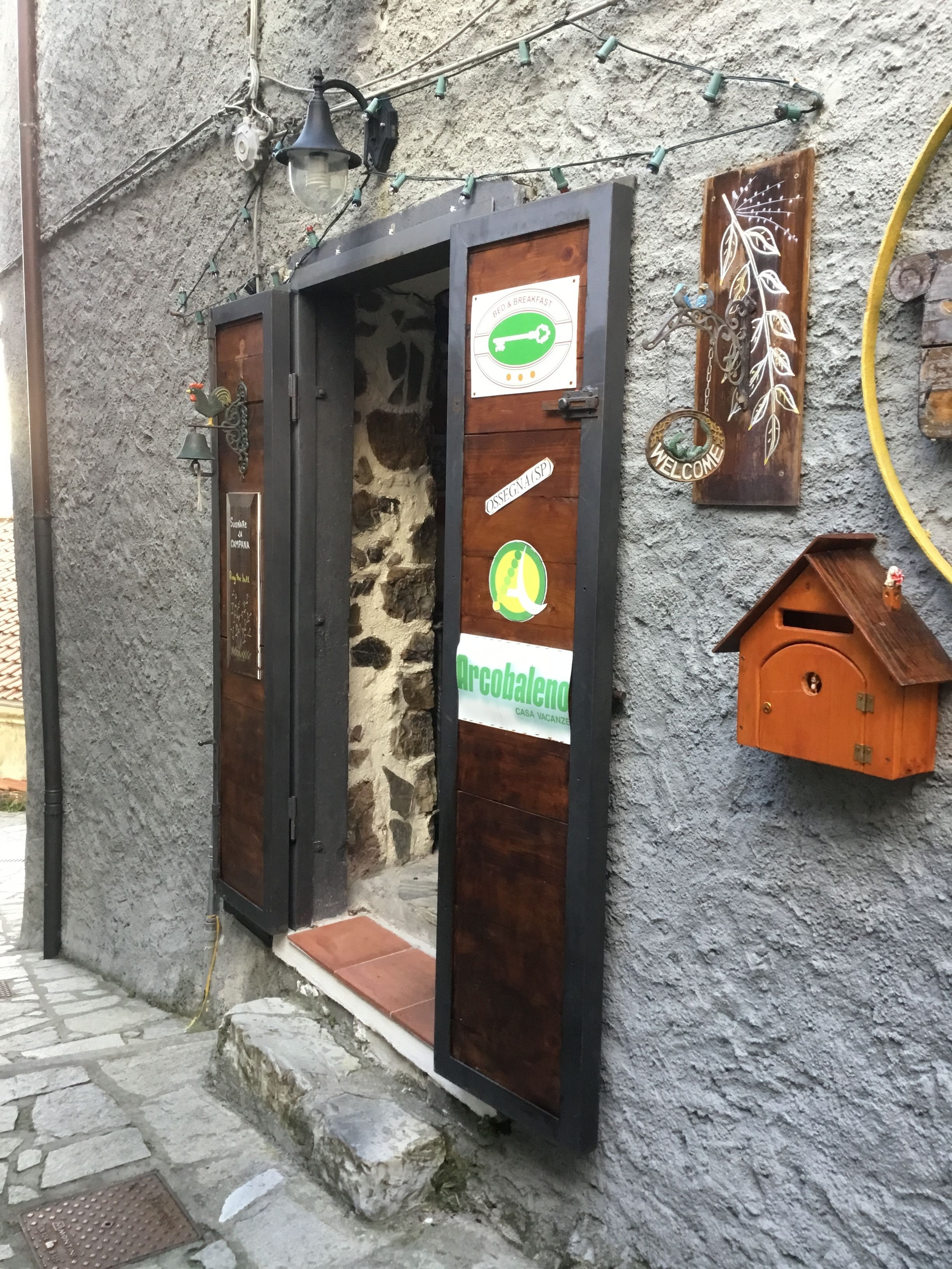 A rustic building with a stone wall exterior, a wooden door with a sign indicating a bed and breakfast, and a small wooden birdhouse attached to the wall.