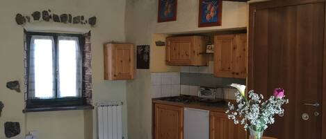 A rustic kitchen with wooden cabinets, a dining table with chairs, and a window with curtains.