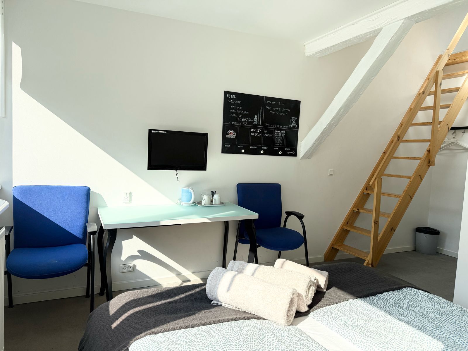 Una habitación pequeña y moderna con un escritorio, dos sillas, un televisor y una escalera.
