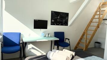 Una habitación pequeña y moderna con un escritorio, dos sillas, un televisor y una escalera.
