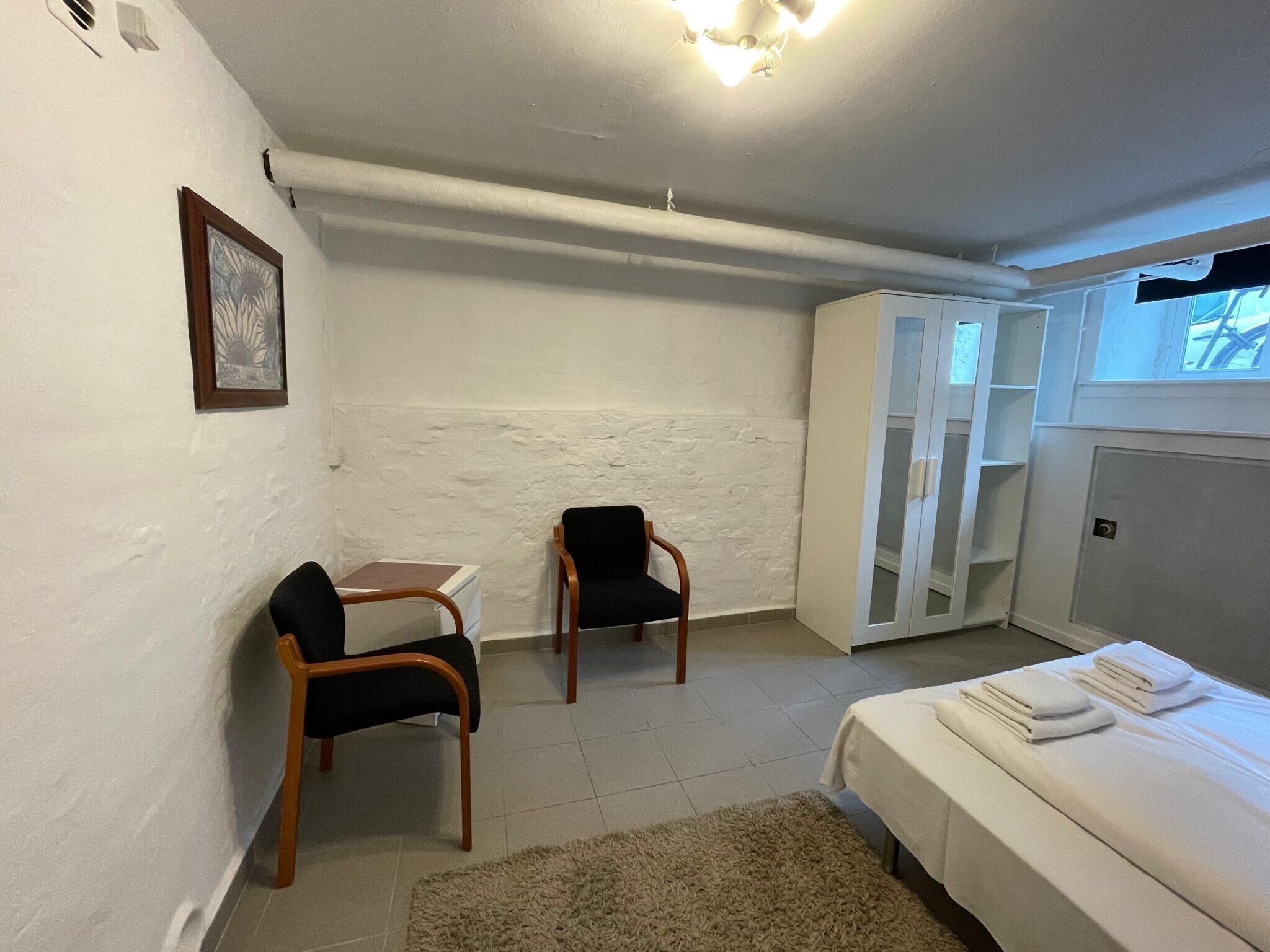 Une chambre à coucher avec un lit, deux chaises, une armoire blanche et une petite table.