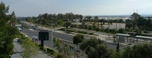 A road with a pedestrian crossing, a sign for 'Posidonia', and a view of the sea and buildings in the distance. - Hotel Ikaros (Elliniko-Argyroupoli)