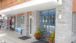 A hotel entrance with a stone facade, a blue door, and flower pots. - Apparthotel Feehof Saas-Fee (Saas-Fee)