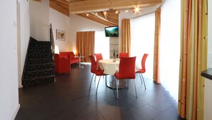 A dining area with a round table, red chairs, a TV on the wall, and a staircase leading to another level. - Apparthotel Feehof Saas-Fee (Saas-Fee)