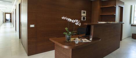 Un mostrador de recepción con detalles de madera, una orquídea en maceta y un vaso de agua.
