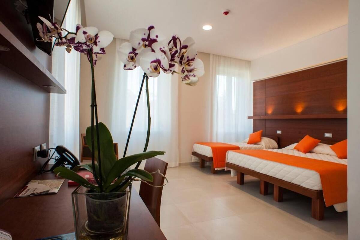 Ein Hotelzimmer mit zwei Betten, einem Holzkopfteil, einem Schreibtisch mit Stuhl und einem Blumentopf.