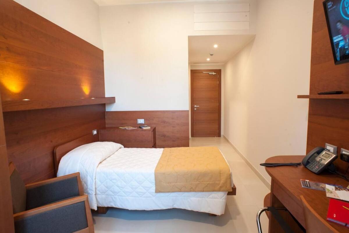 Ein Hotelzimmer mit Bett, Nachttisch und Schreibtisch, inklusive Telefon und rotem Ordner.