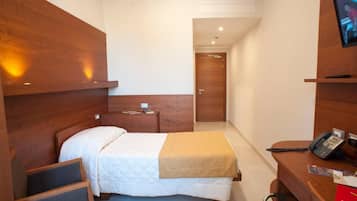 Une chambre d’hôtel avec un lit, une table de chevet et un bureau équipé d’un téléphone et d’un classeur rouge.
