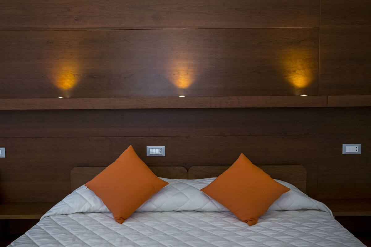 Ein Schlafzimmer mit einem Holzkopfteil, zwei orangefarbenen Kissen und einer weißen, gesteppten Bettdecke.