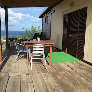 A wooden deck with a table and chairs, a green mat, and a view of the ocean.